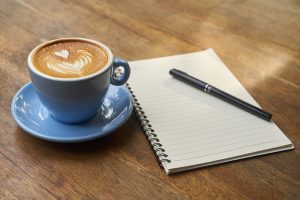 Cup of frothy coffee next to a notebook