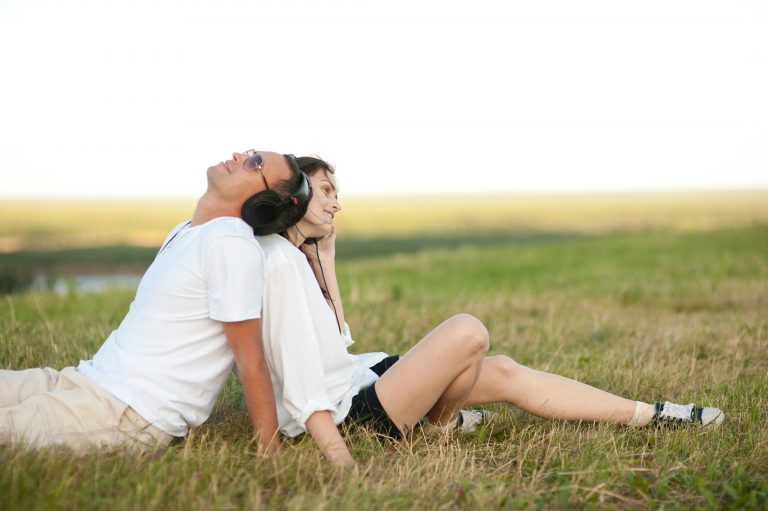 Happy young couple listening to music together in a field