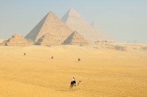 A figure on a camel with Egyptian pyramids in the distance